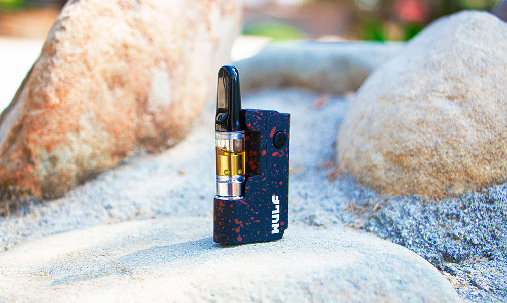 WULF Micro Plus 510 thread battery in black with red spatter, standing on a rock with a cartridge attached
