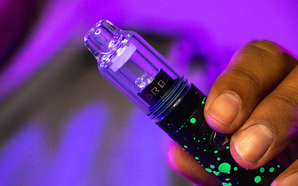 Hand holding a WULF Orbit concentrate vaporizer under purple lighting