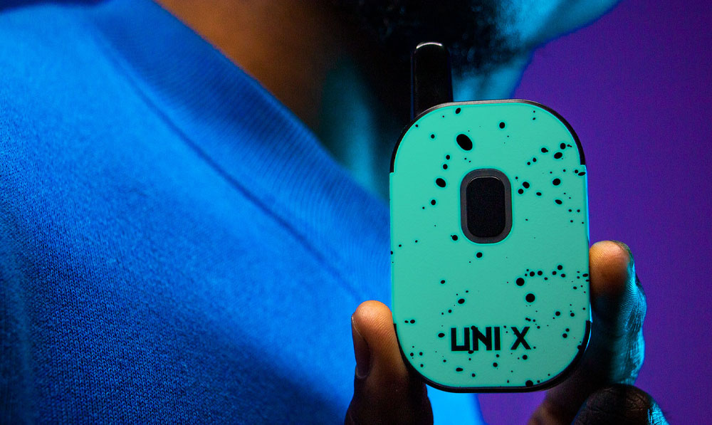 Teal Black Spatter Wulf UNI X in man's hands against purple studio background