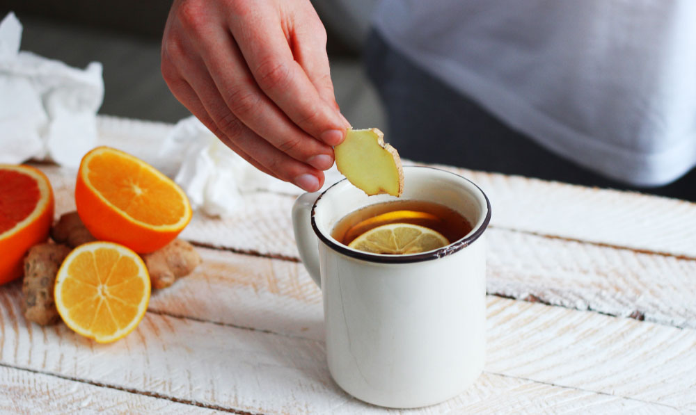Man dipping something into cup of tea with oranges nearby