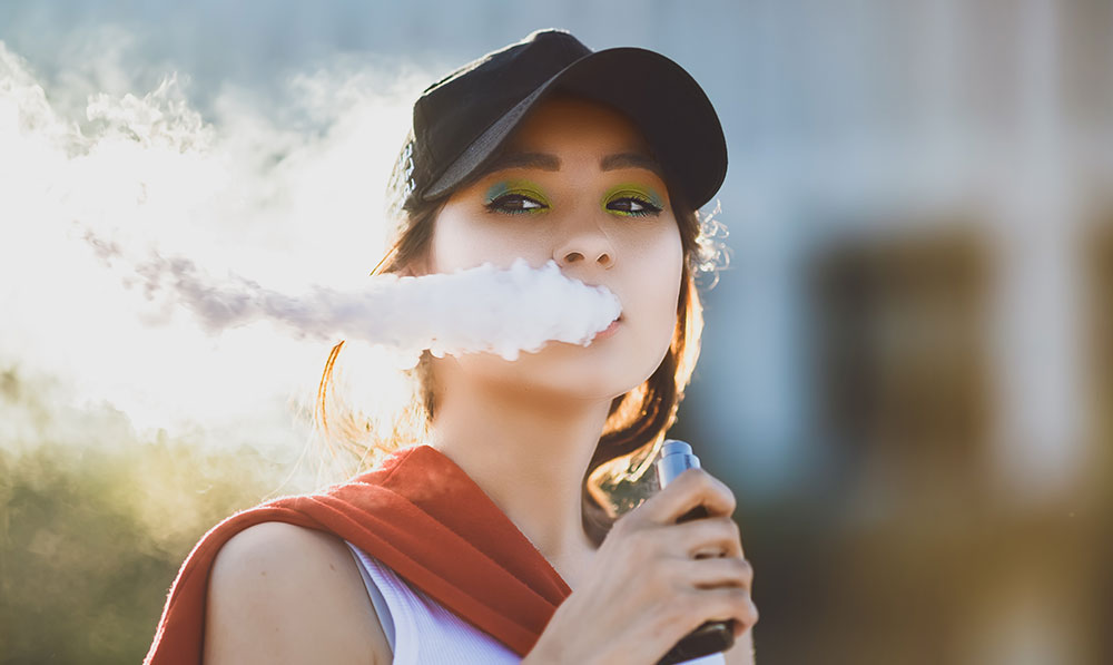 Asian woman in baseball cap vaping outside