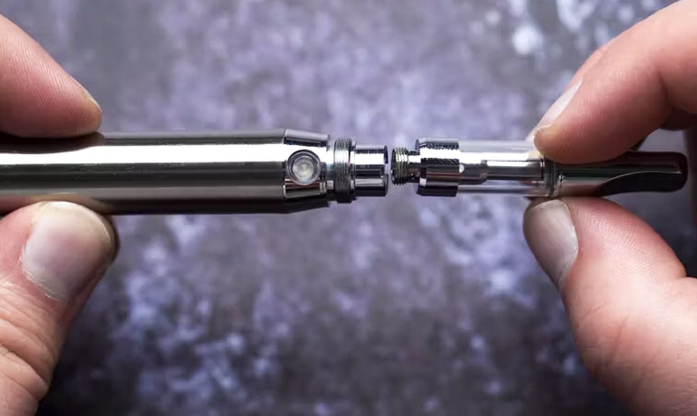 Person preparing to screw vape cartridge into vaporizer