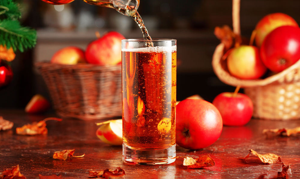 Apple Cider on wooden desk with apples and Christmas tree nearby