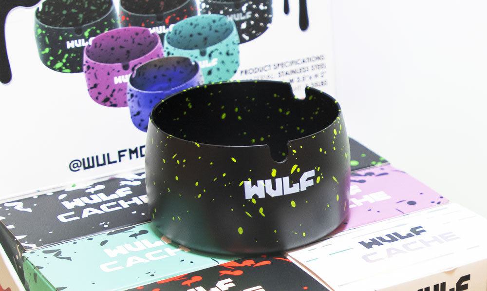 WULF Cache ashtray in black with green spatter beside its retail packaging
