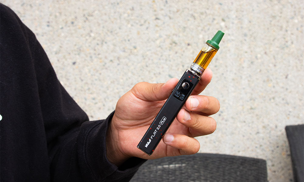 Hand holding a black WULF Flat Plus 510 thread battery with a cartridge attached