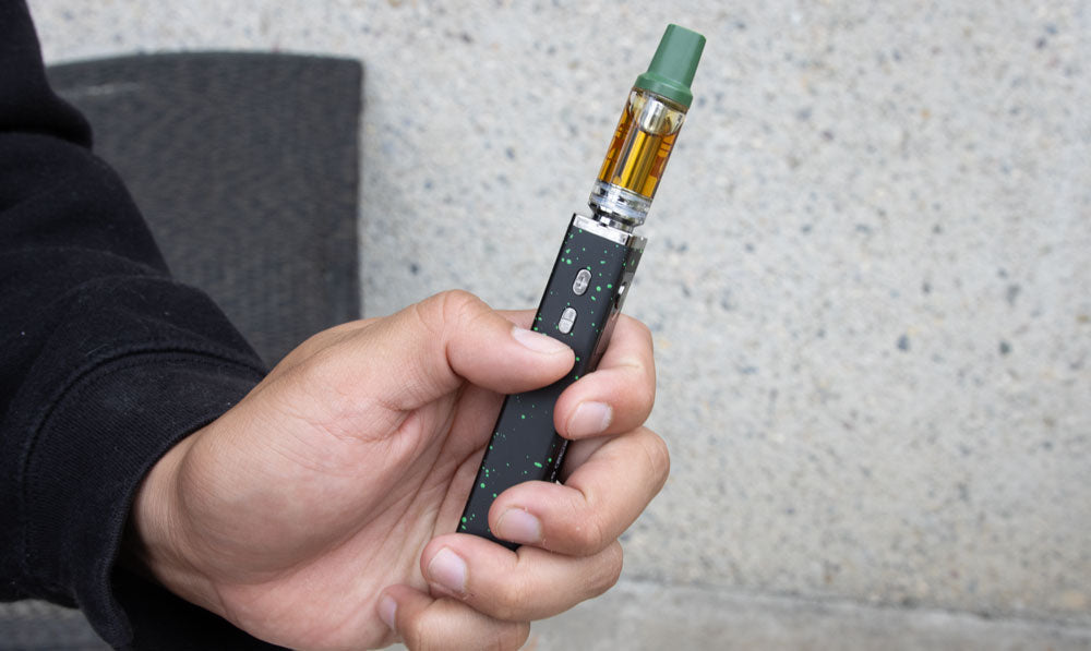 Person holding a black WULF Flat Plus 510 thread battery with a cartridge attached