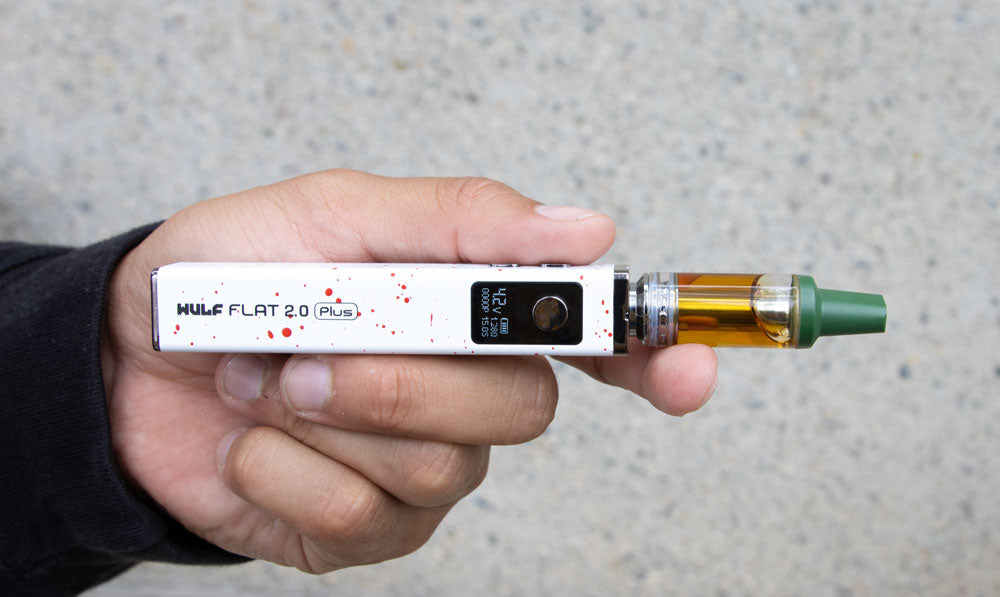 Hand holding a WULF Flat Plus 510 thread battery in white with red spatter