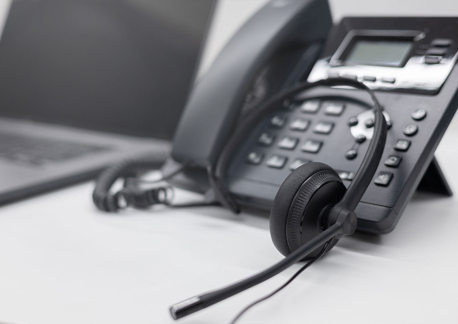 Desk phone with a headset resting on it beside a laptop