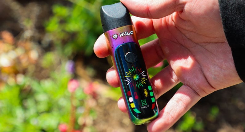 Hands holding a rainbow WULF Budr portable concentrate vaporizer outdoors