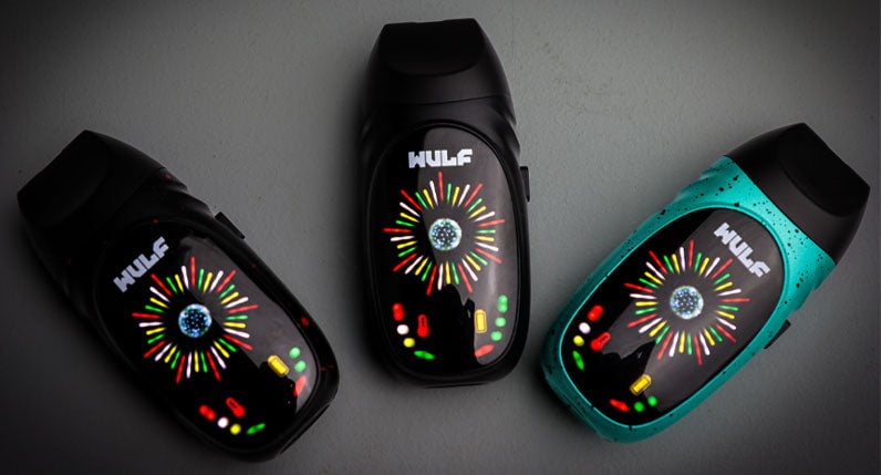 Three WULF Faze portable dry herb vaporizers in black, white and teal on a dark surface