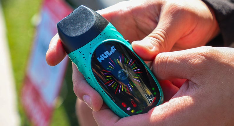 Hand holding a teal WULF Faze portable dry herb vaporizer outdoors