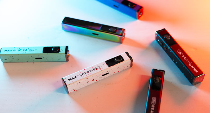 Group of Wulf Mods Flat Mini 2.0 Variable Voltage Batteries on white surface with colorful lighting