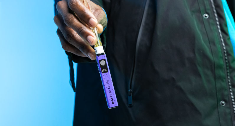 Hand holding a purple WULF Flat Mini 2.0 510 thread battery against a blue background